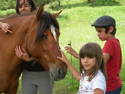Eine Frau umarmt ein Pferd, während es von zwei Kindern am Kopf gestreichelt wird.